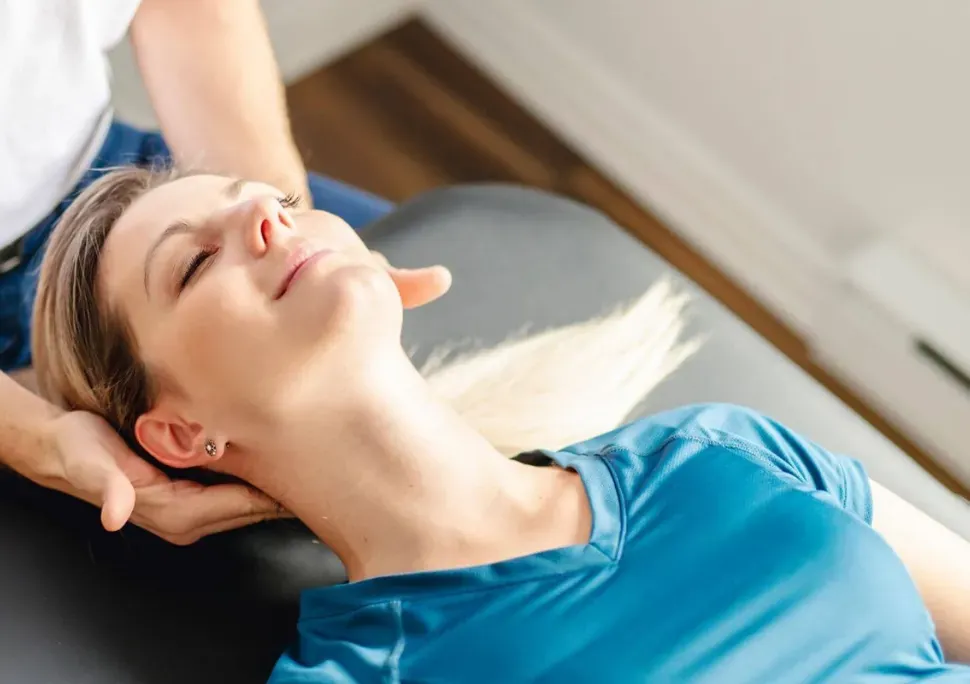 Physical therapist performing hands-on jaw and neck treatment on a patient lying on a treatment table